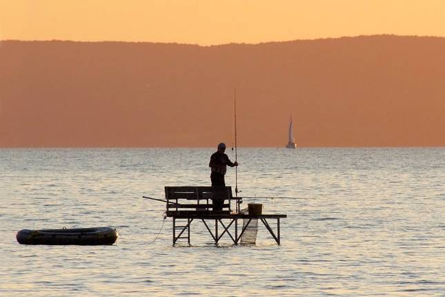 Horgász a naplementében a Balatonon.