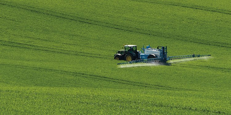 Kék traktor permetezőgéppel permetez a szántóföldön