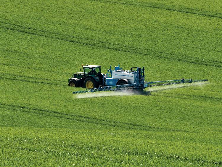 Traktor permetezőgéppel permetez a szántóföldön